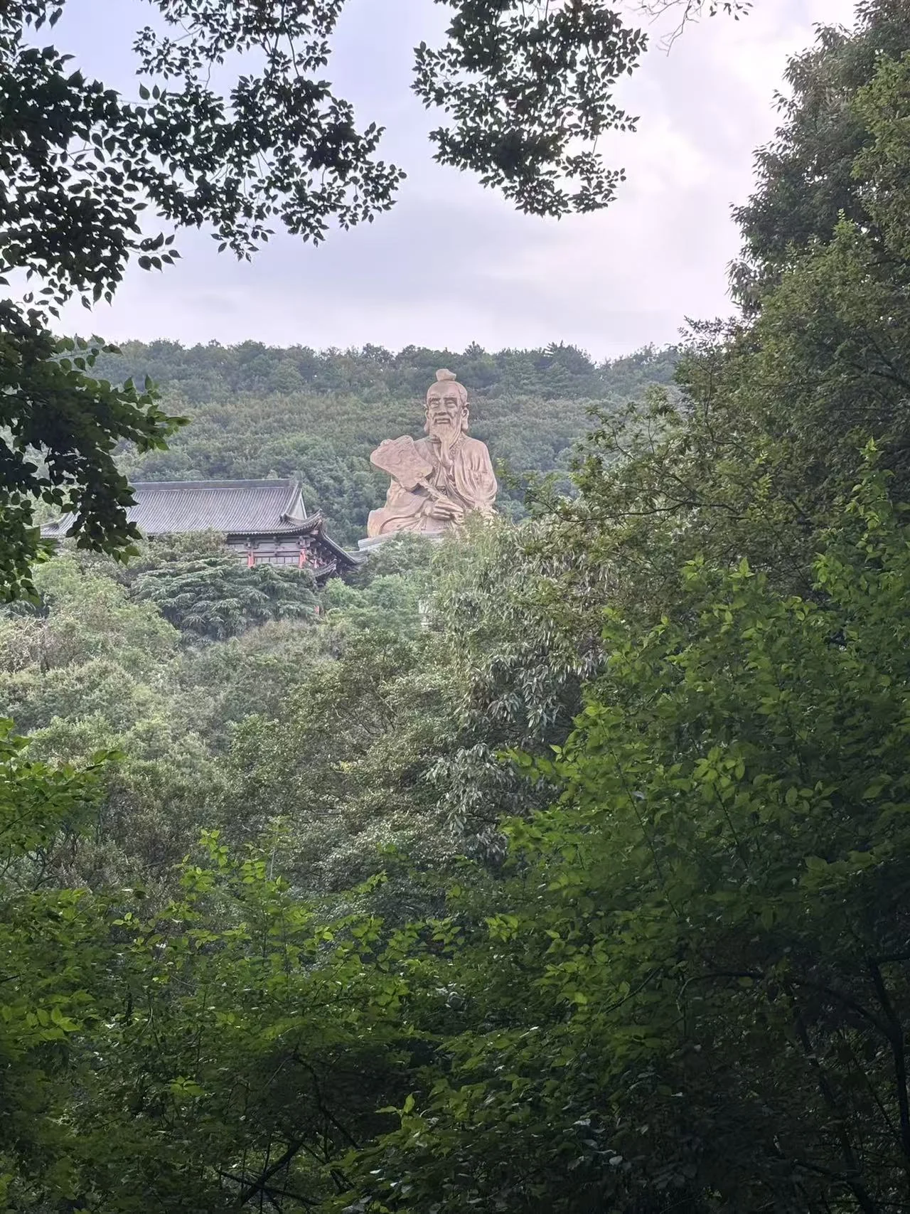 A large seated figure and temple rooftops seen through trees