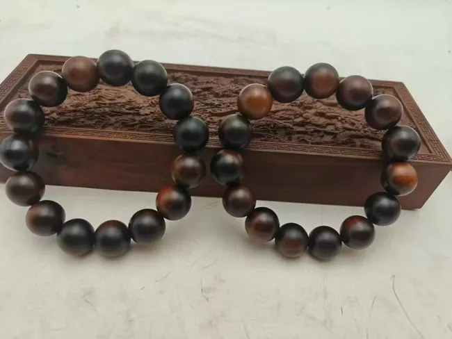 Two dark bead bracelets arranged beside a carved display support.