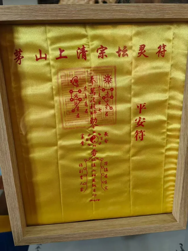 A framed yellow talisman work labelled ping’an fu.