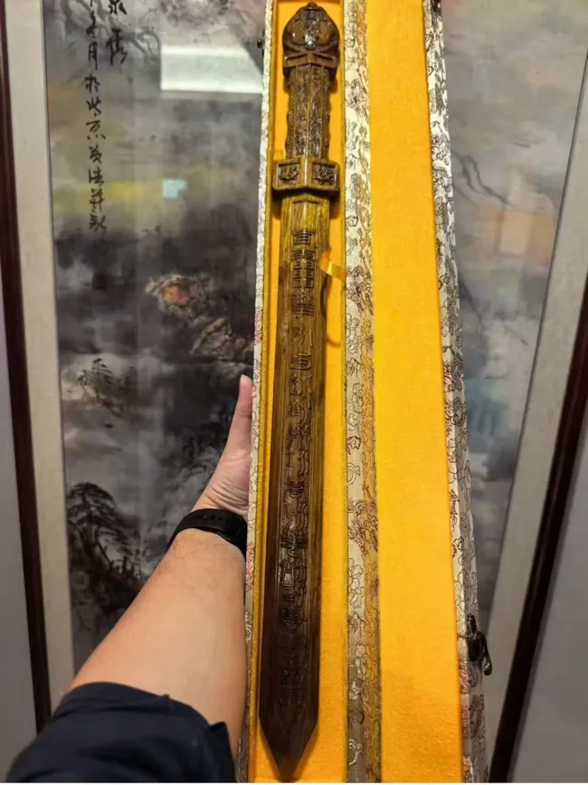 A long sword-shaped object shown in a narrow yellow-lined case.