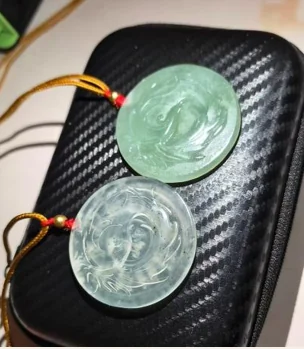 Two green-toned circular carved pendants with cords